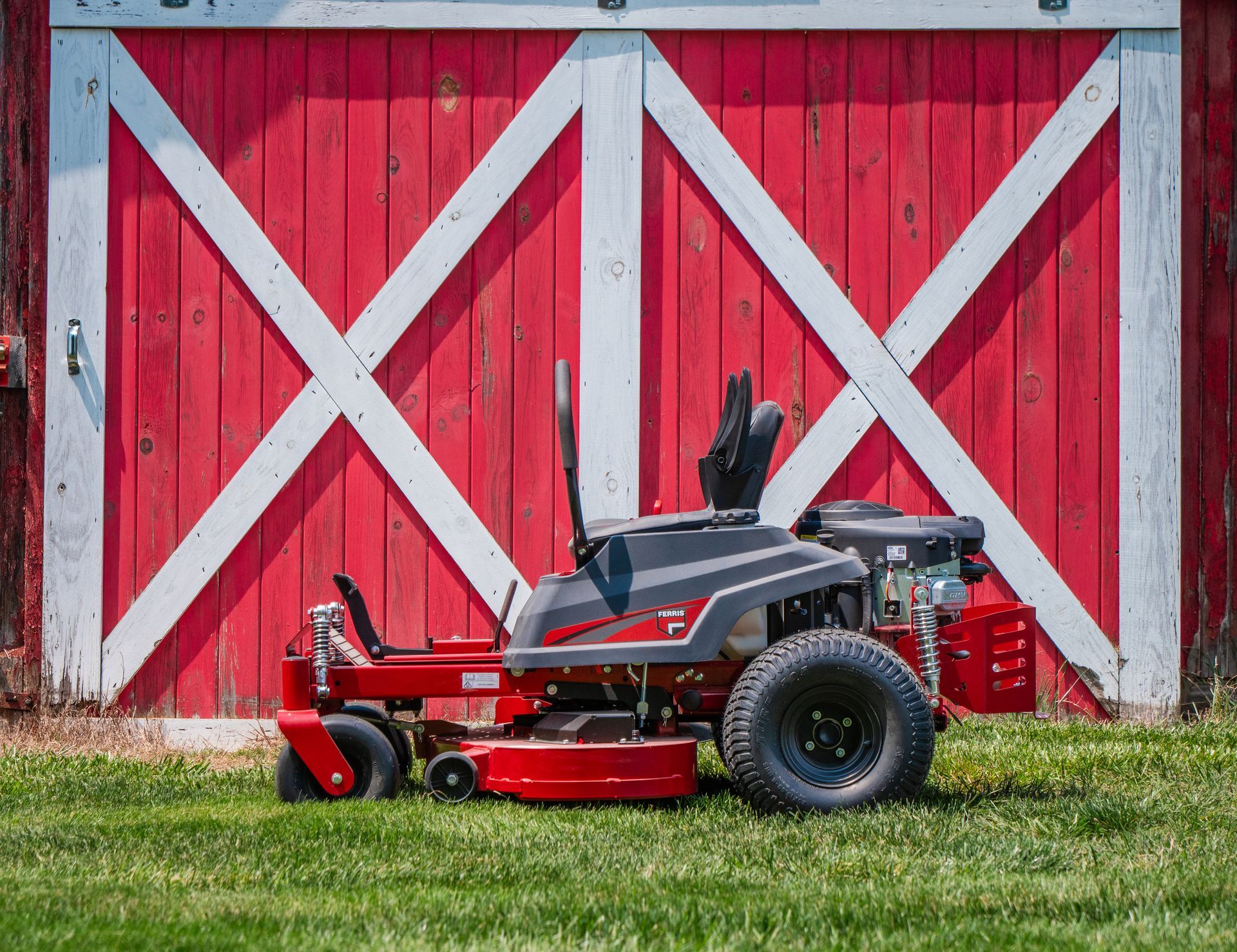 A red and white lawn mower is parked in front of a red barn.