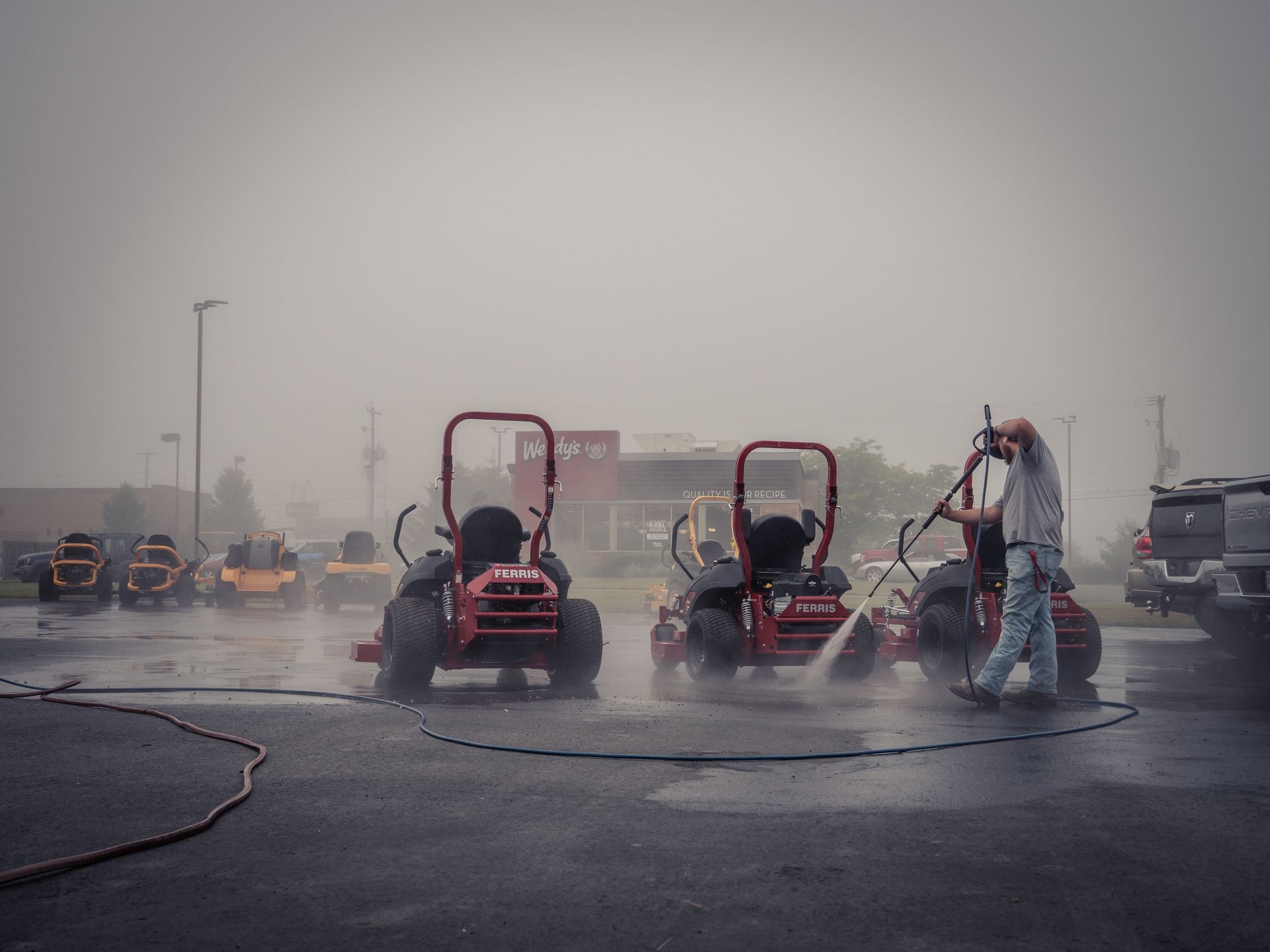 A man is washing a lawn mower in a parking lot.