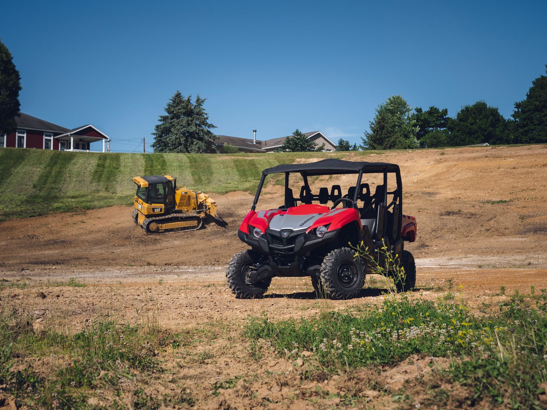 A red atv is parked in a dirt field next to a bulldozer.