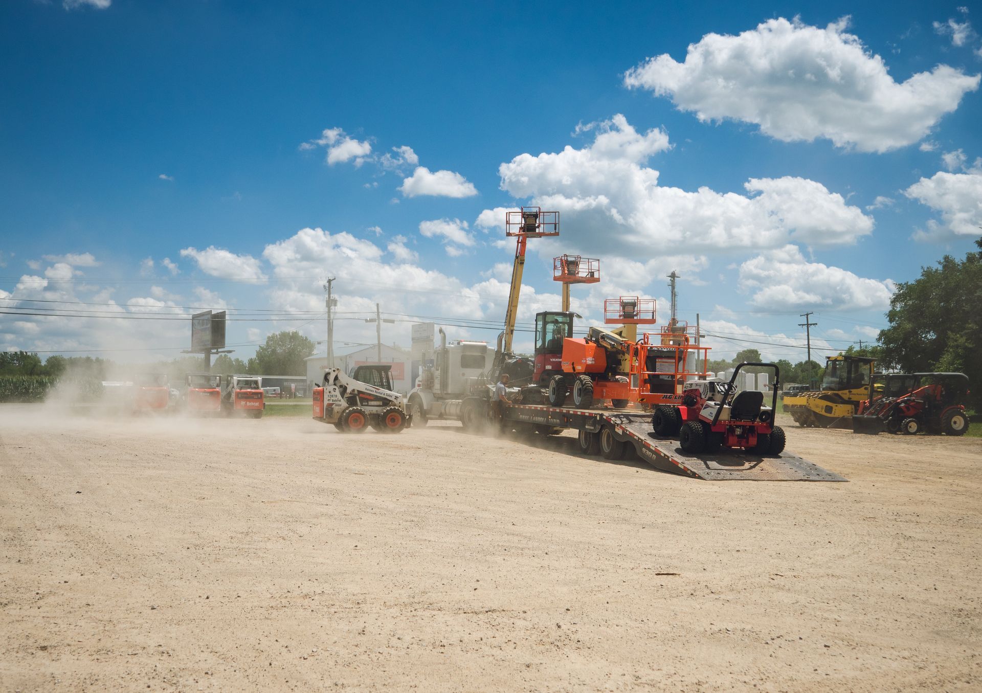 A group of construction vehicles are parked in a dirt lot.