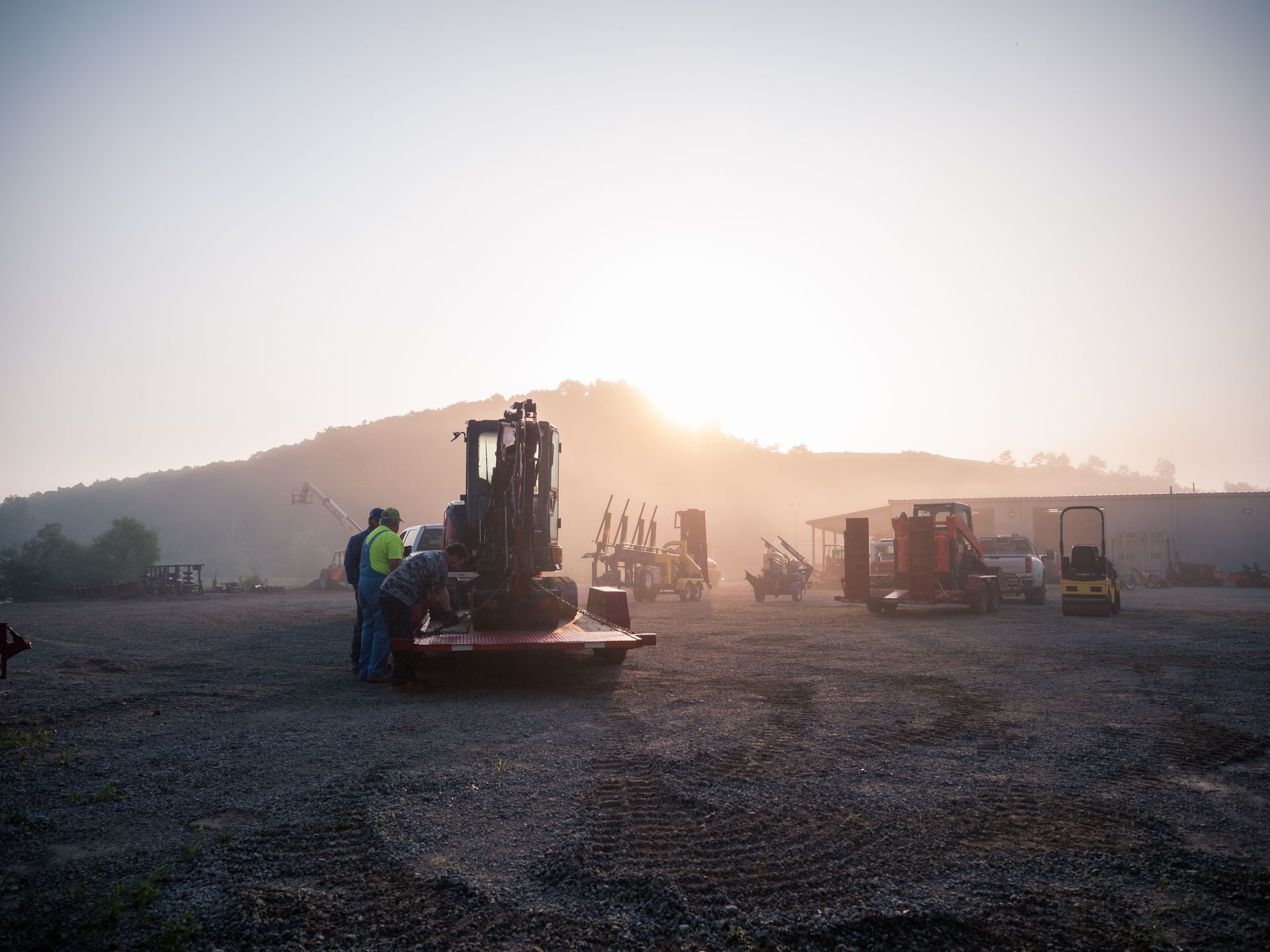 A group of people are working on a forklift in a parking lot at sunset.