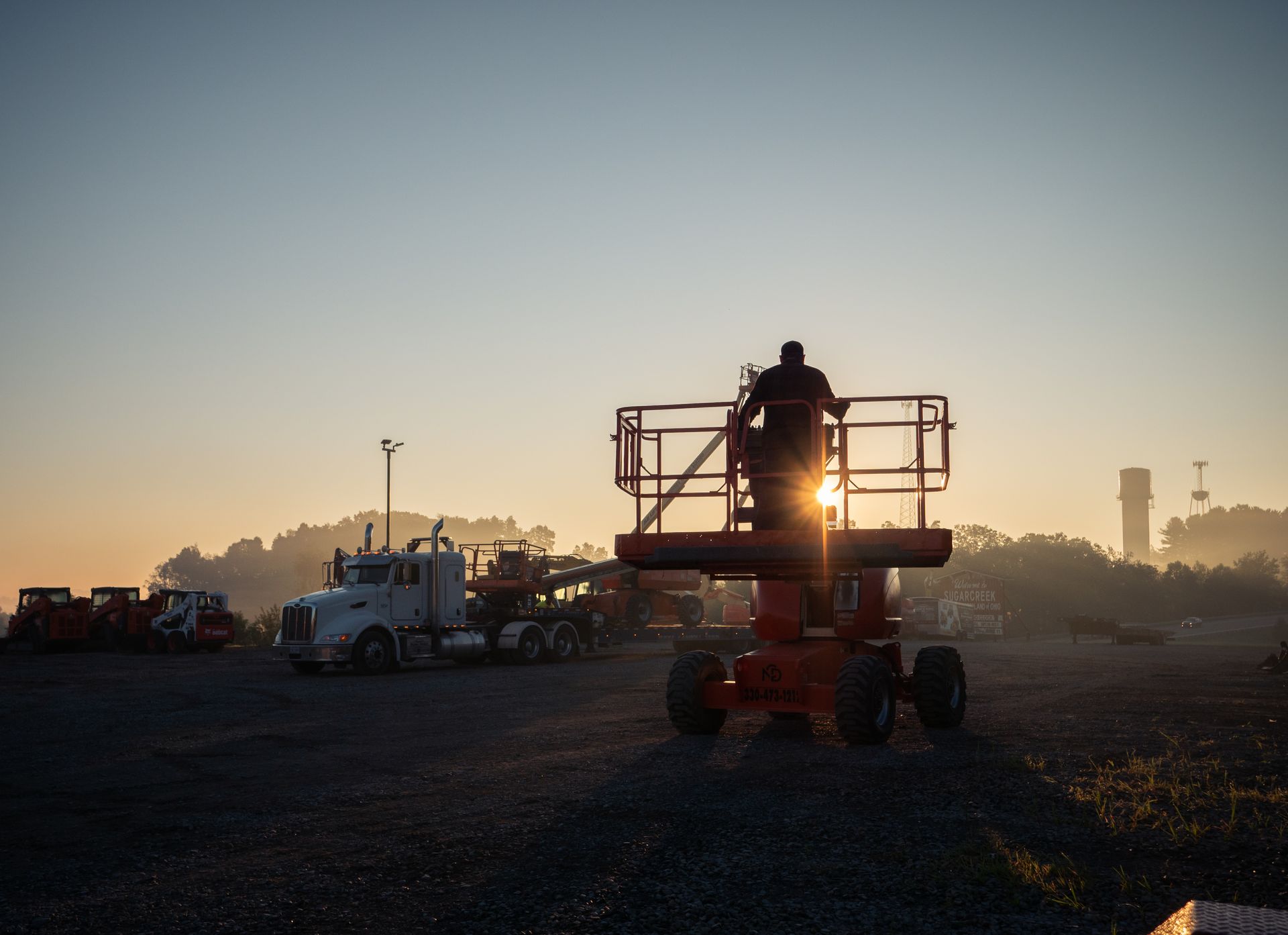 A man is standing on a lift in a parking lot at sunset.