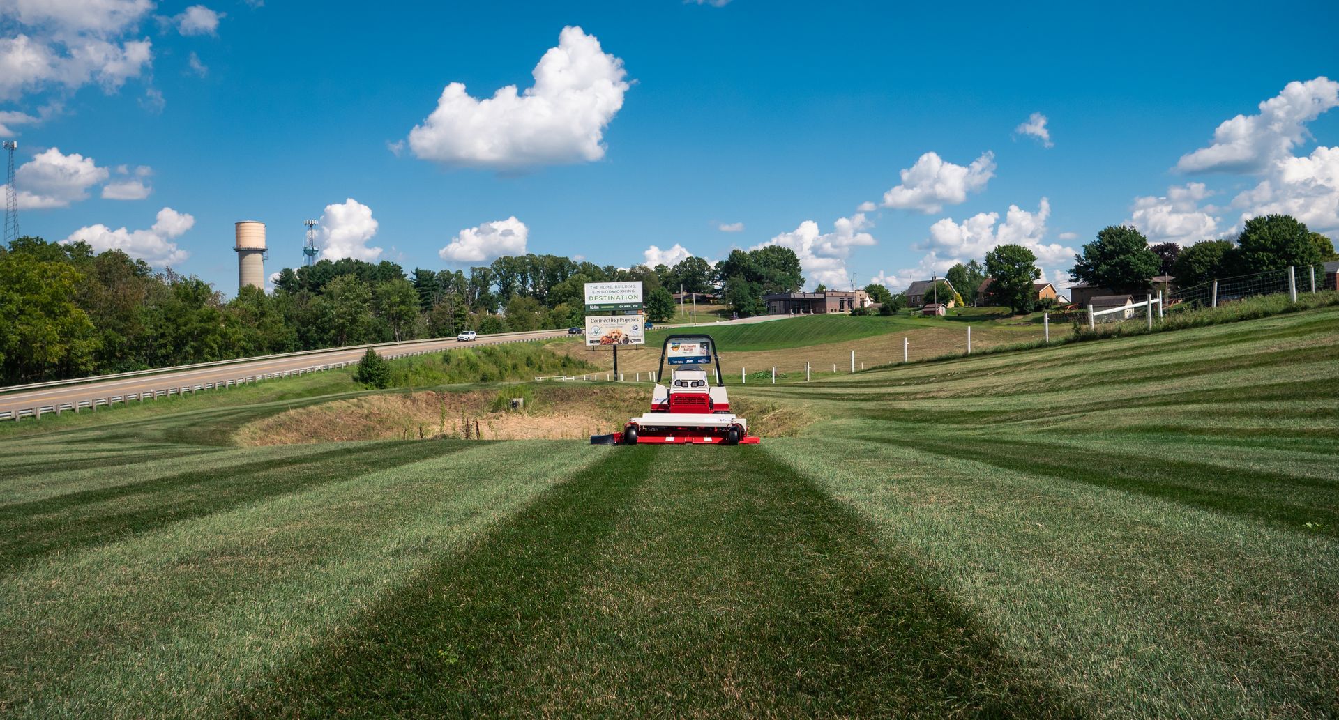 A lawn mower is cutting grass in a field on a sunny day.