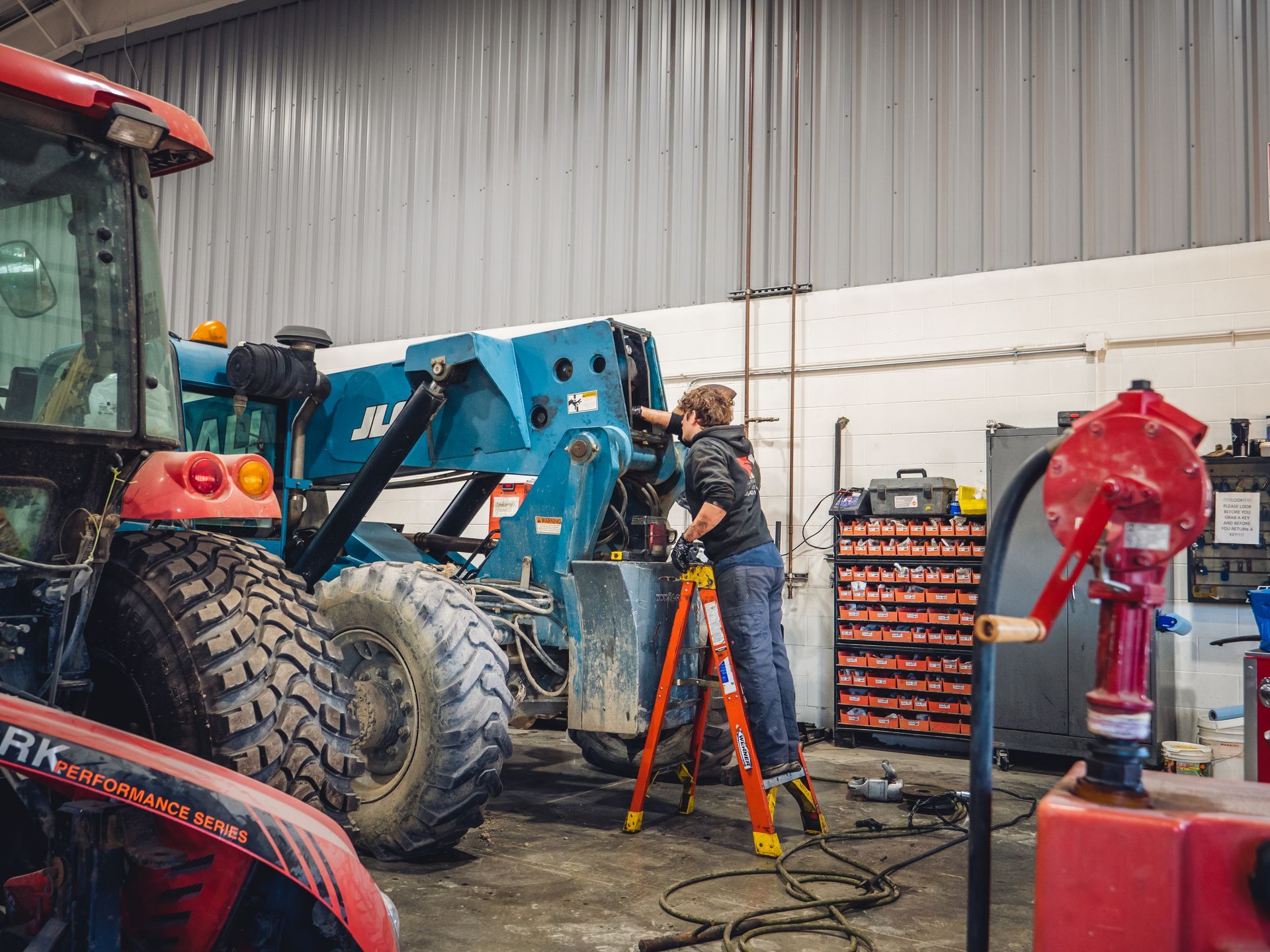 A man is standing on a ladder working on a tractor in a garage.