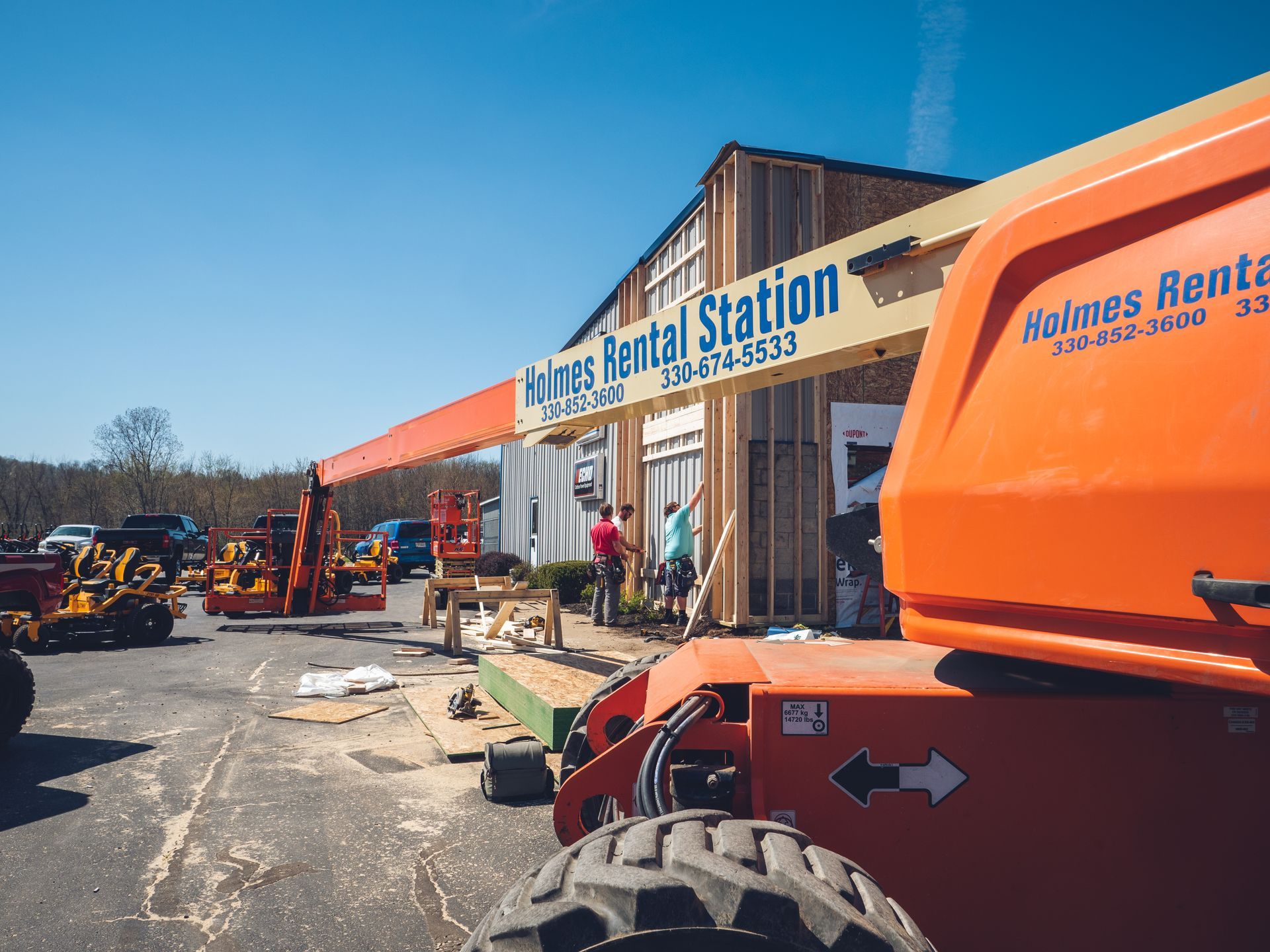 An orange jlg lift is parked in front of a building that says rental station