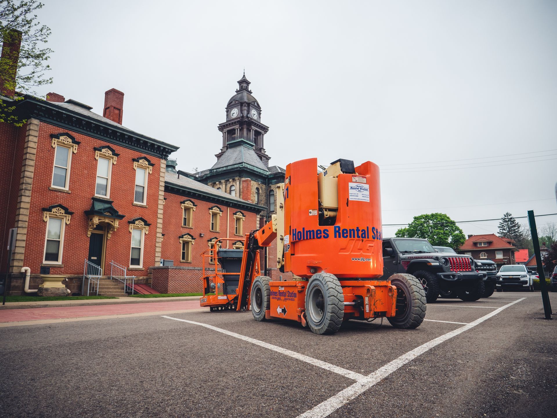 An orange lift is parked in a parking lot in front of a large brick building.
