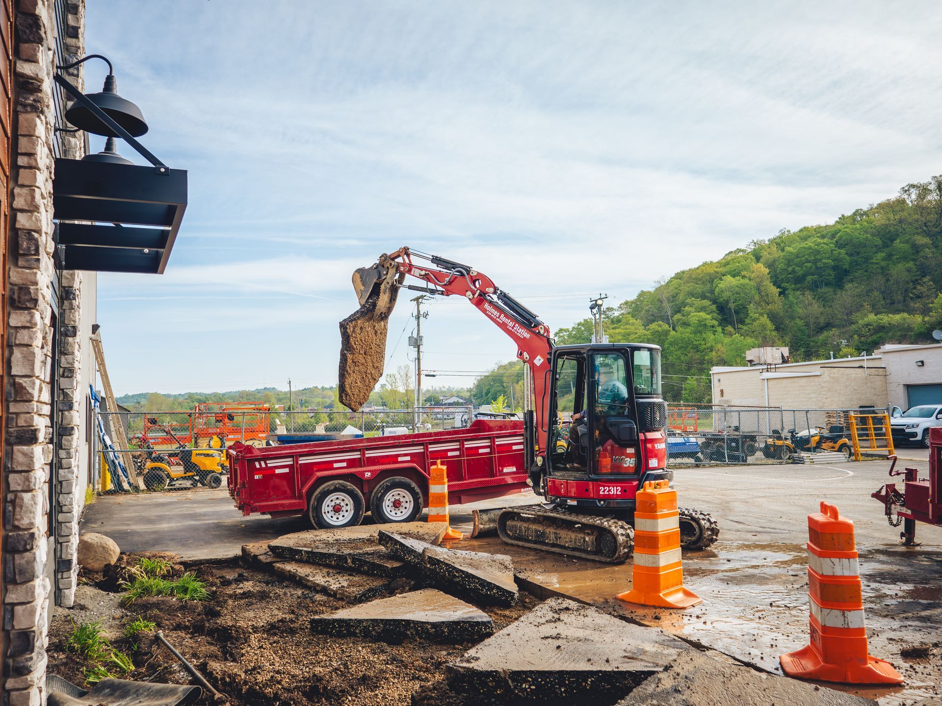 A red excavator is digging a hole in a parking lot.