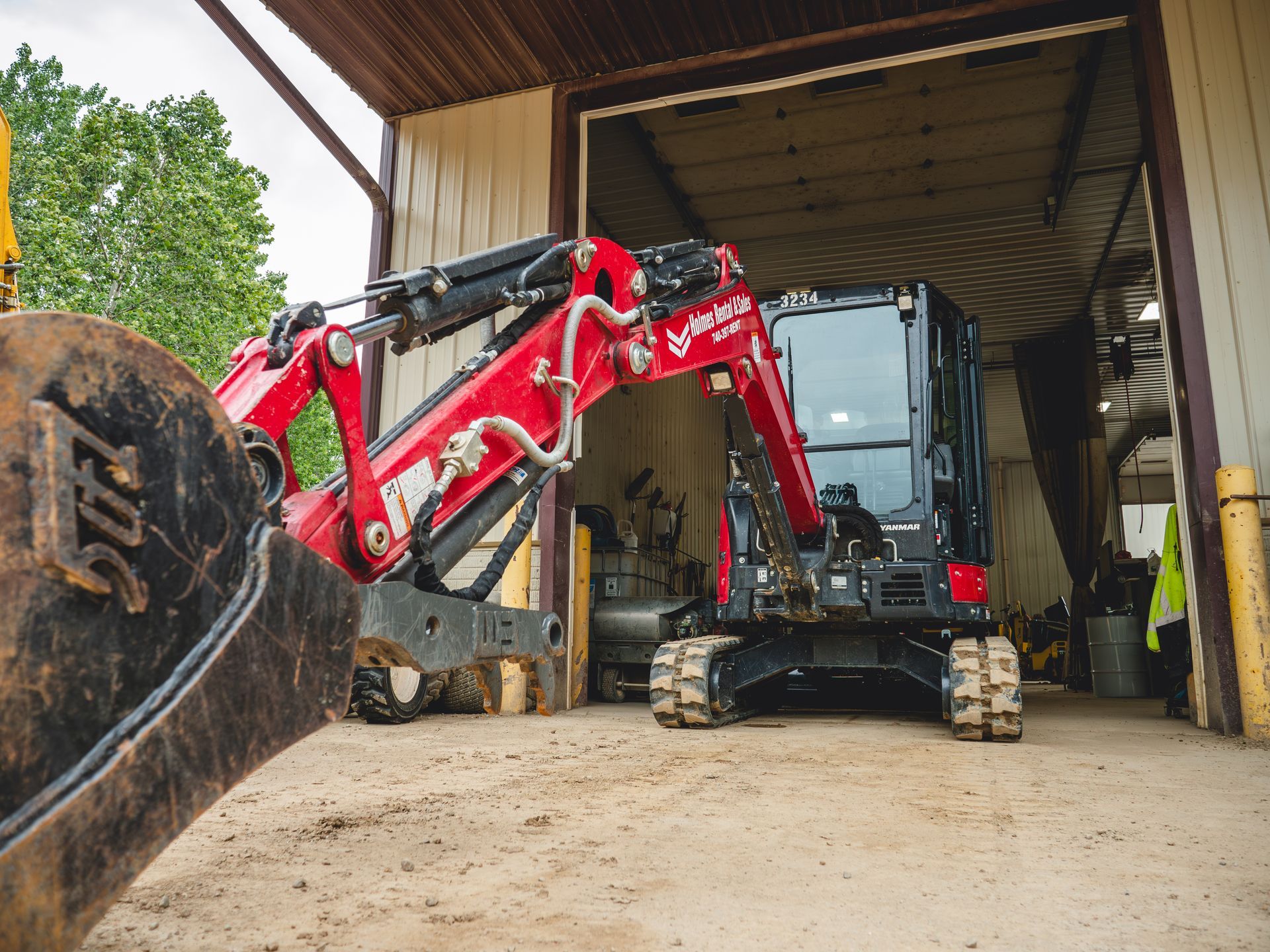 A red and black excavator is parked in a garage.