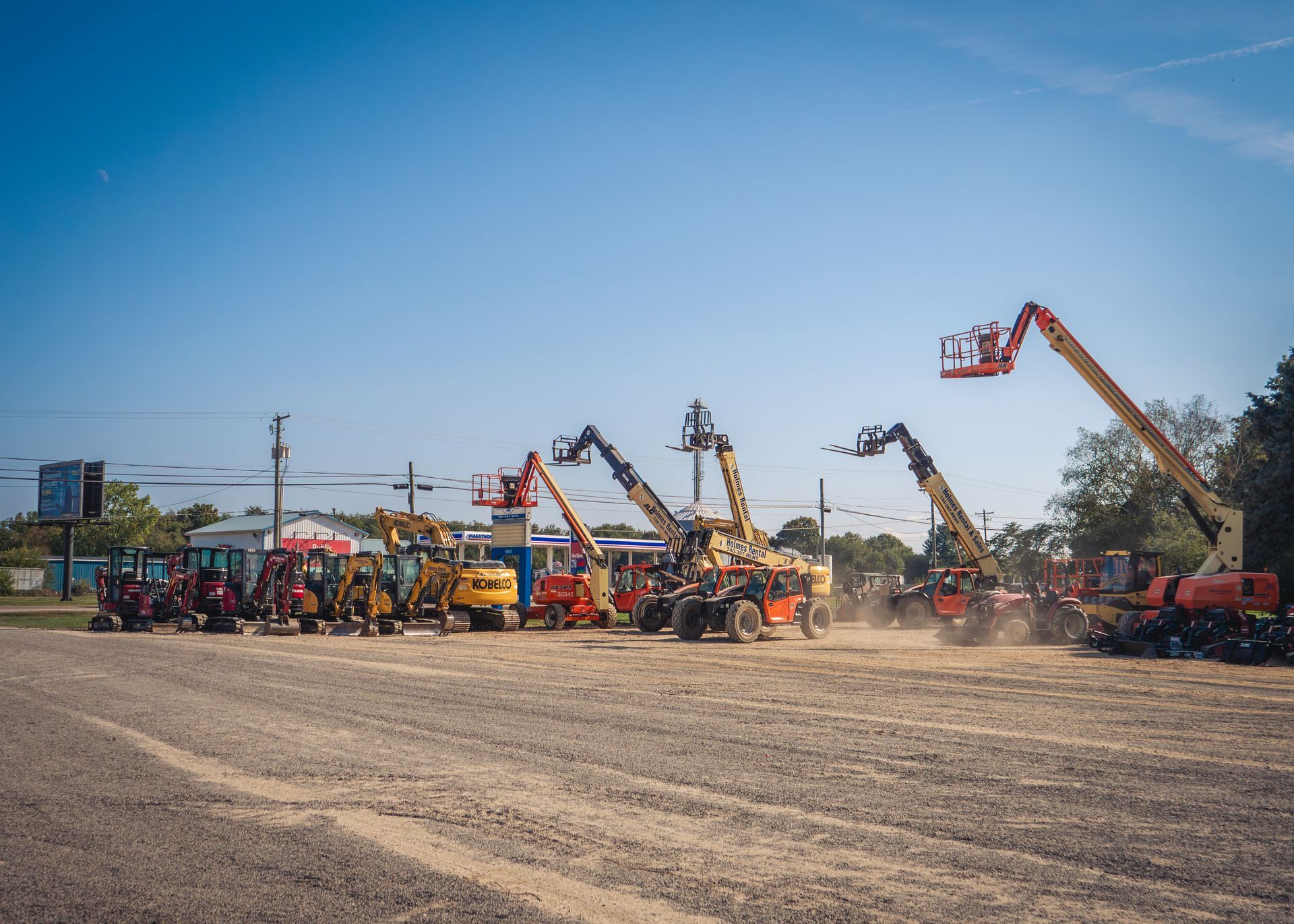 A row of construction vehicles are parked in a dirt lot.