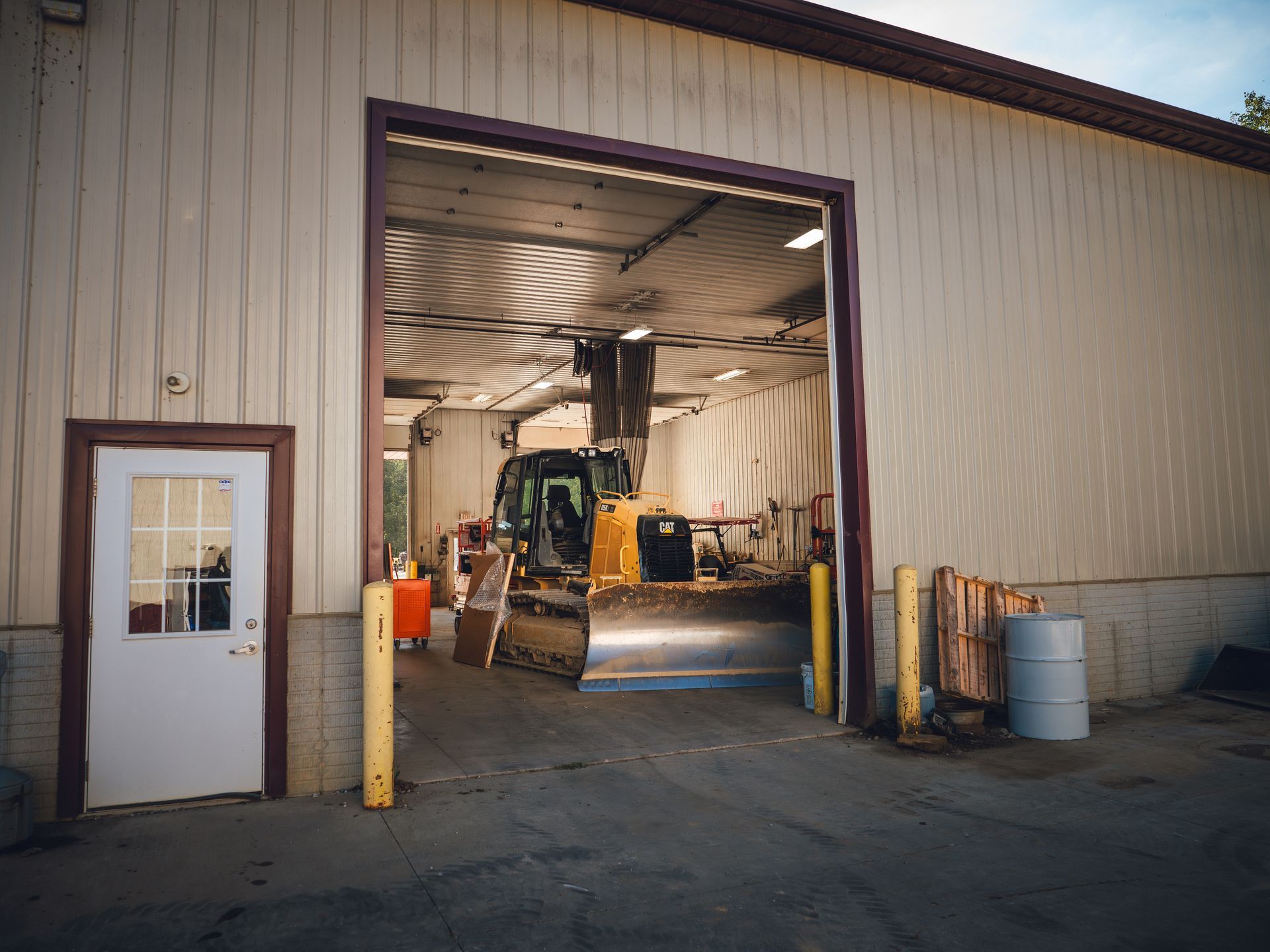 A bulldozer is parked in a garage with the door open.