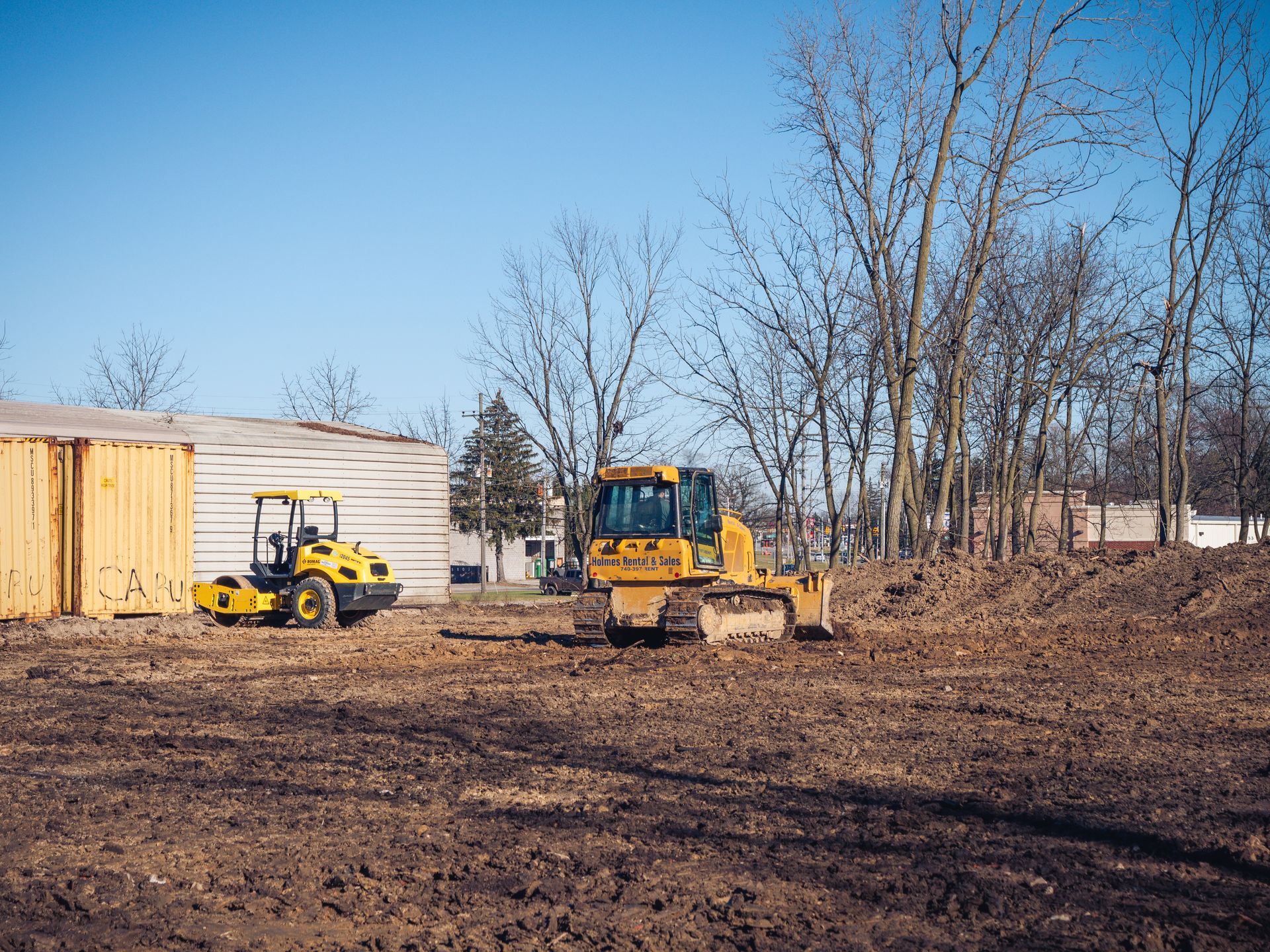A bulldozer and a roller are sitting in a dirt field.