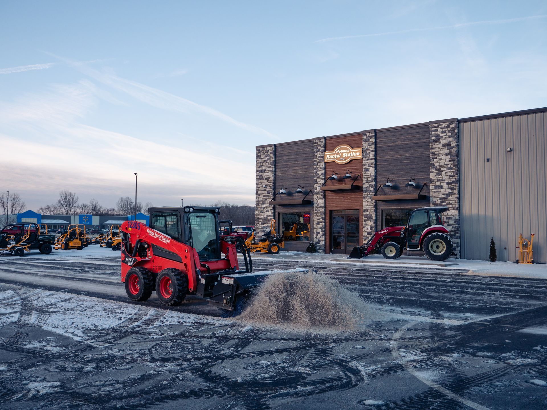 A red tractor is plowing snow in front of a building.