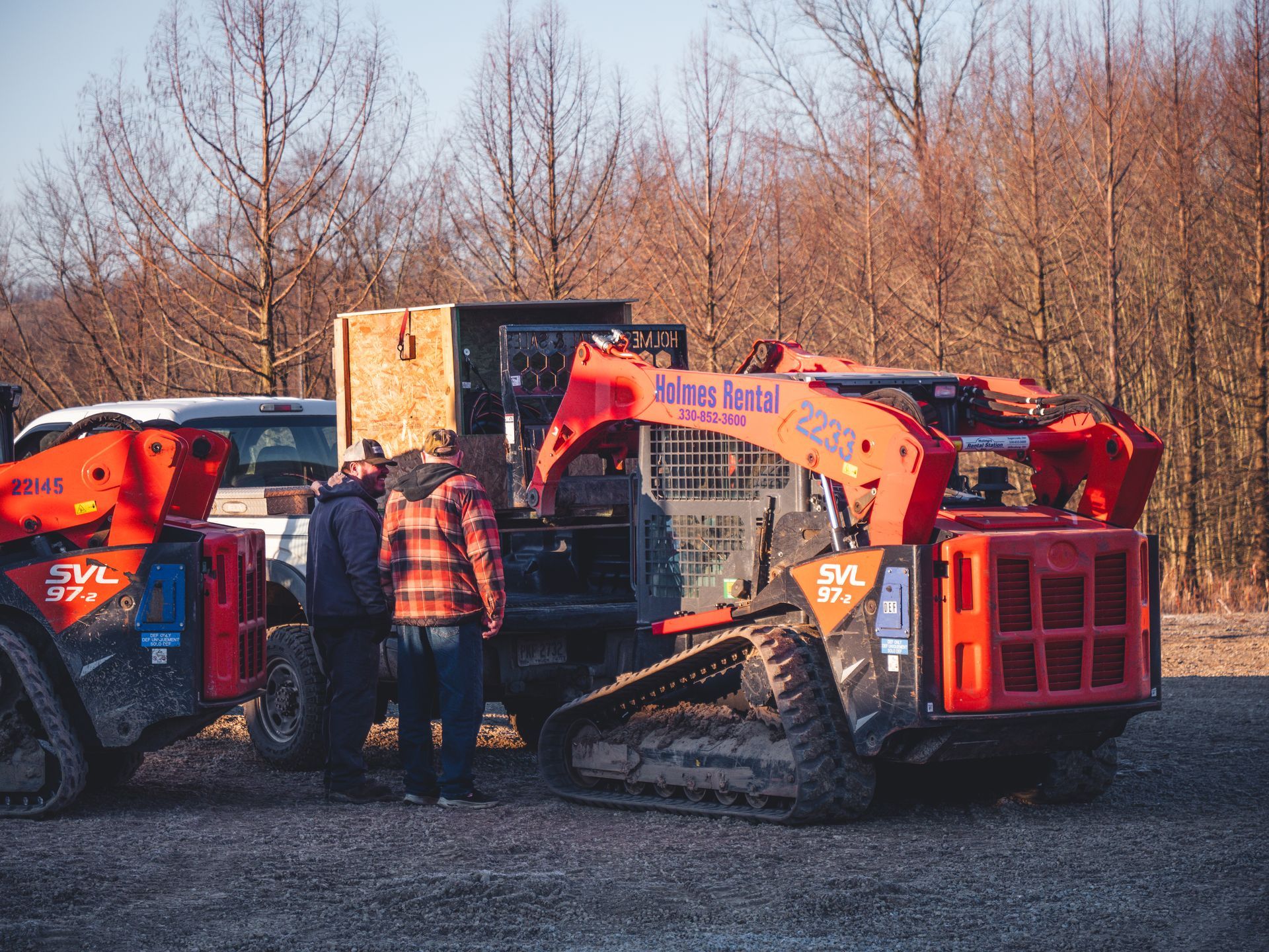 A group of men are standing next to a red bulldozer in a gravel lot.