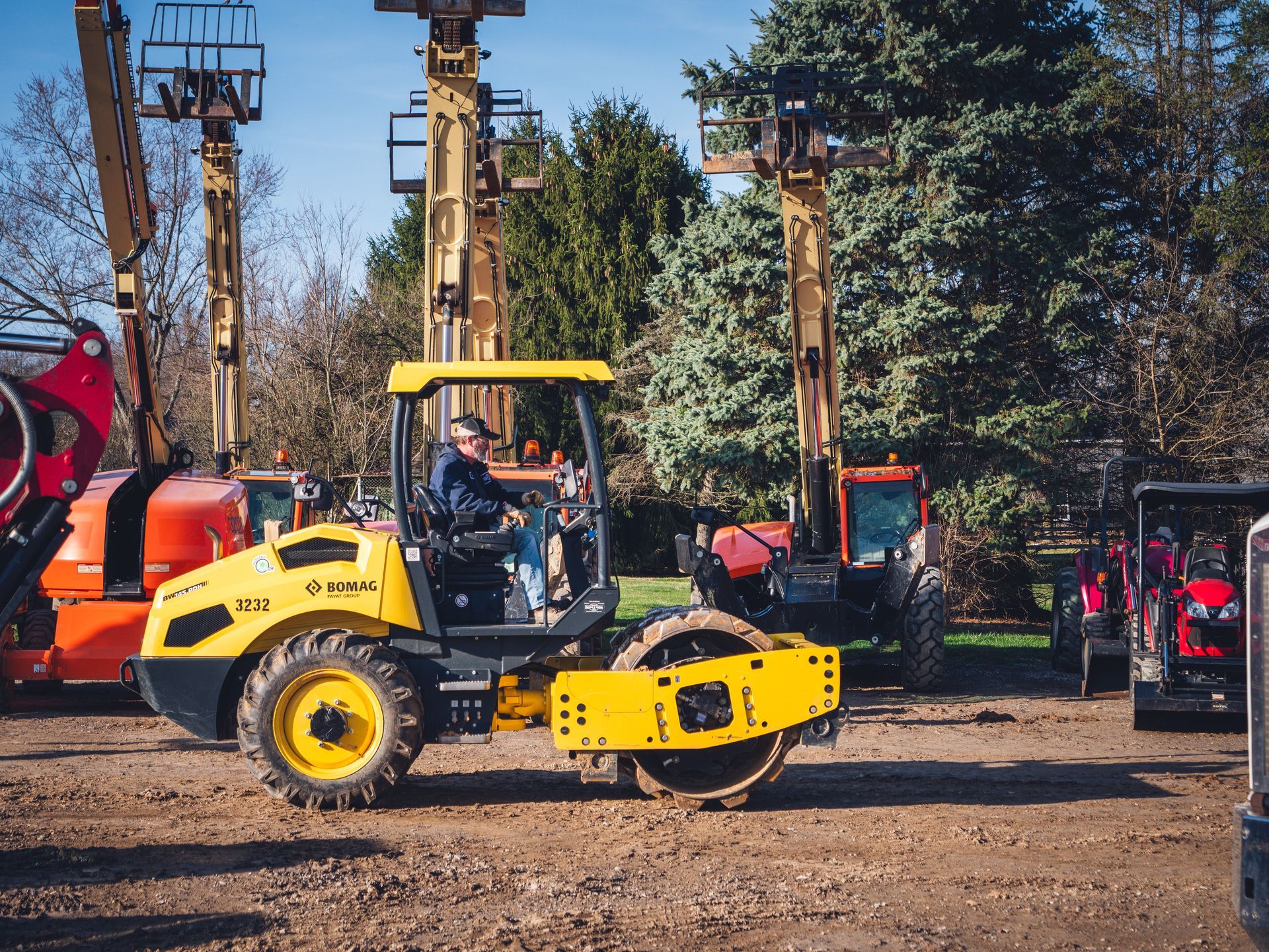 A man is driving a yellow and black tractor on a dirt road.