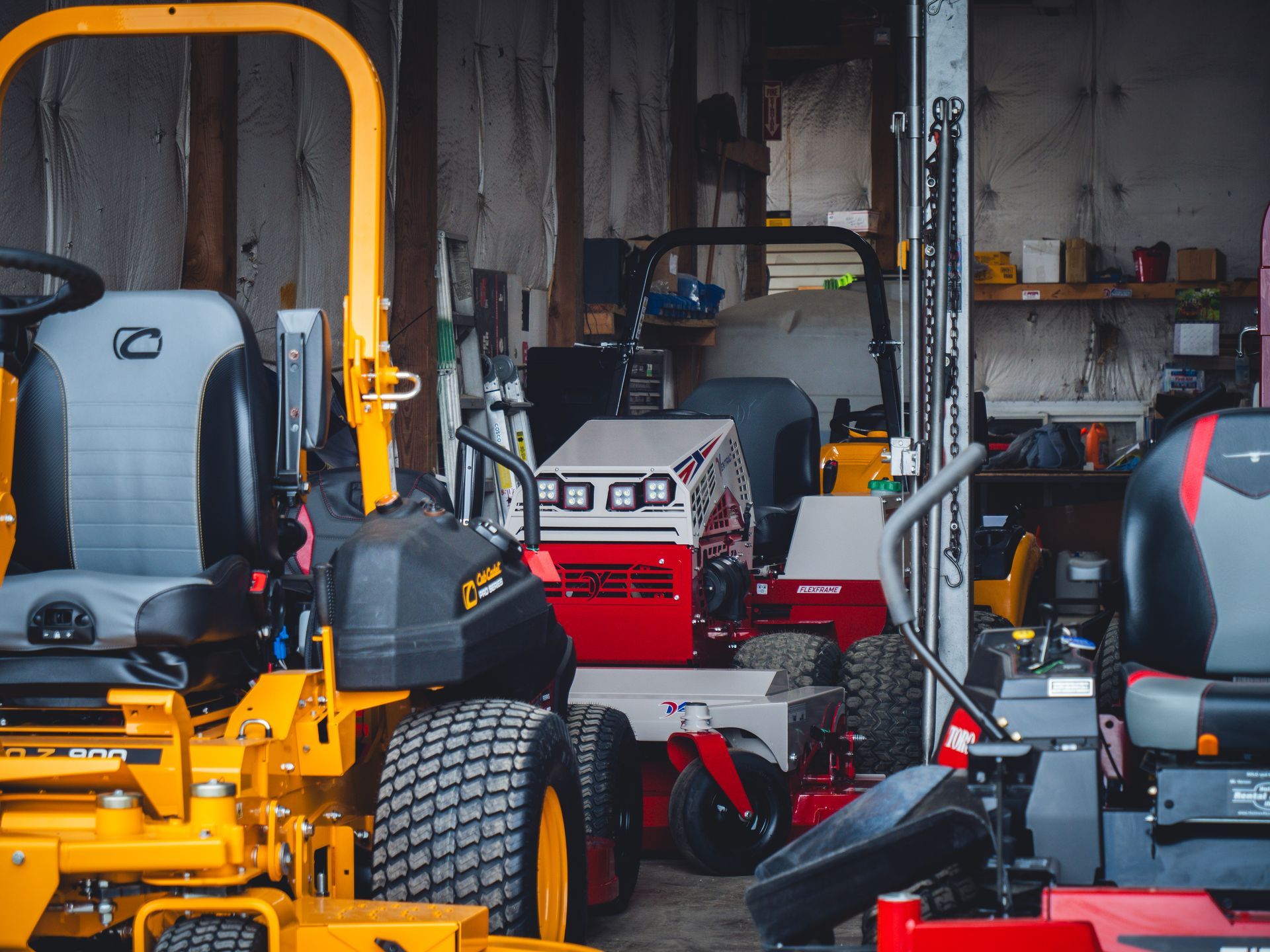 A bunch of lawn mowers are parked in a garage.