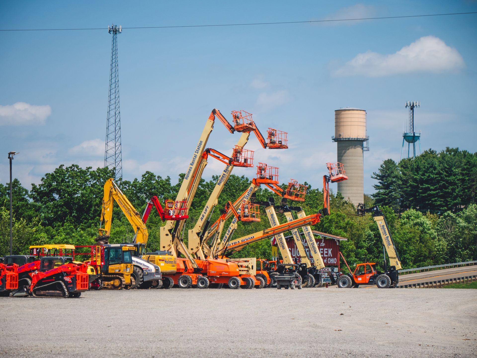 A row of construction vehicles are parked in a gravel lot.