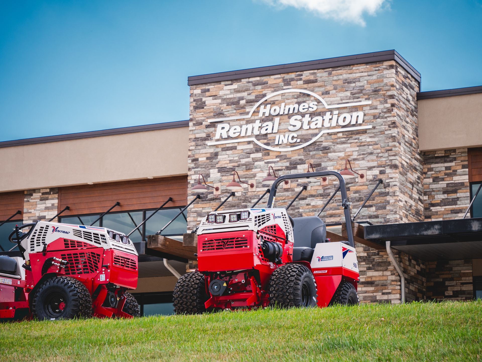 Two red lawn mowers are parked in front of a rental station.