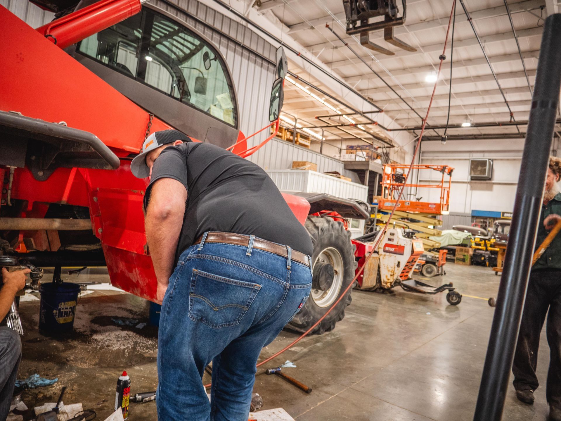 A man is working on a red tractor in a garage.