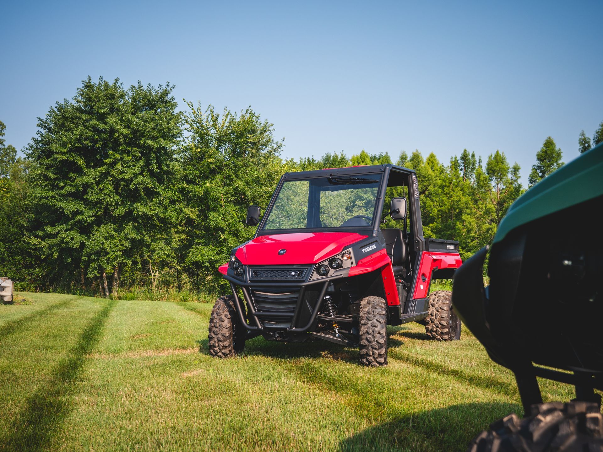 A red atv is parked in a grassy field next to a green tractor.