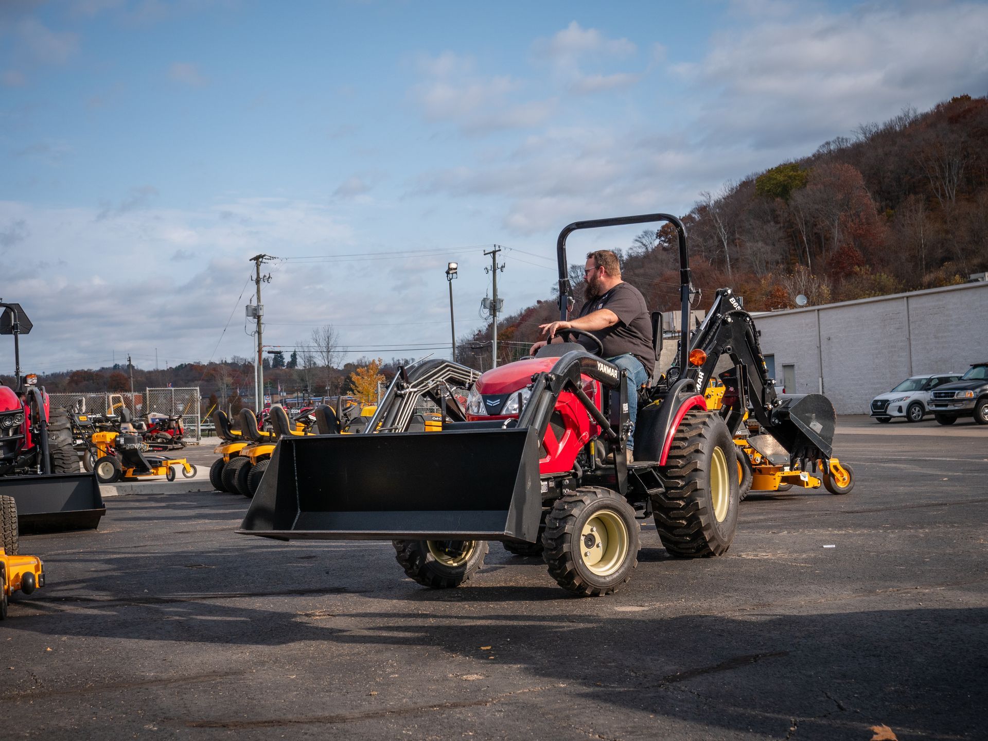A man is driving a tractor with a bucket attached to it in a parking lot.