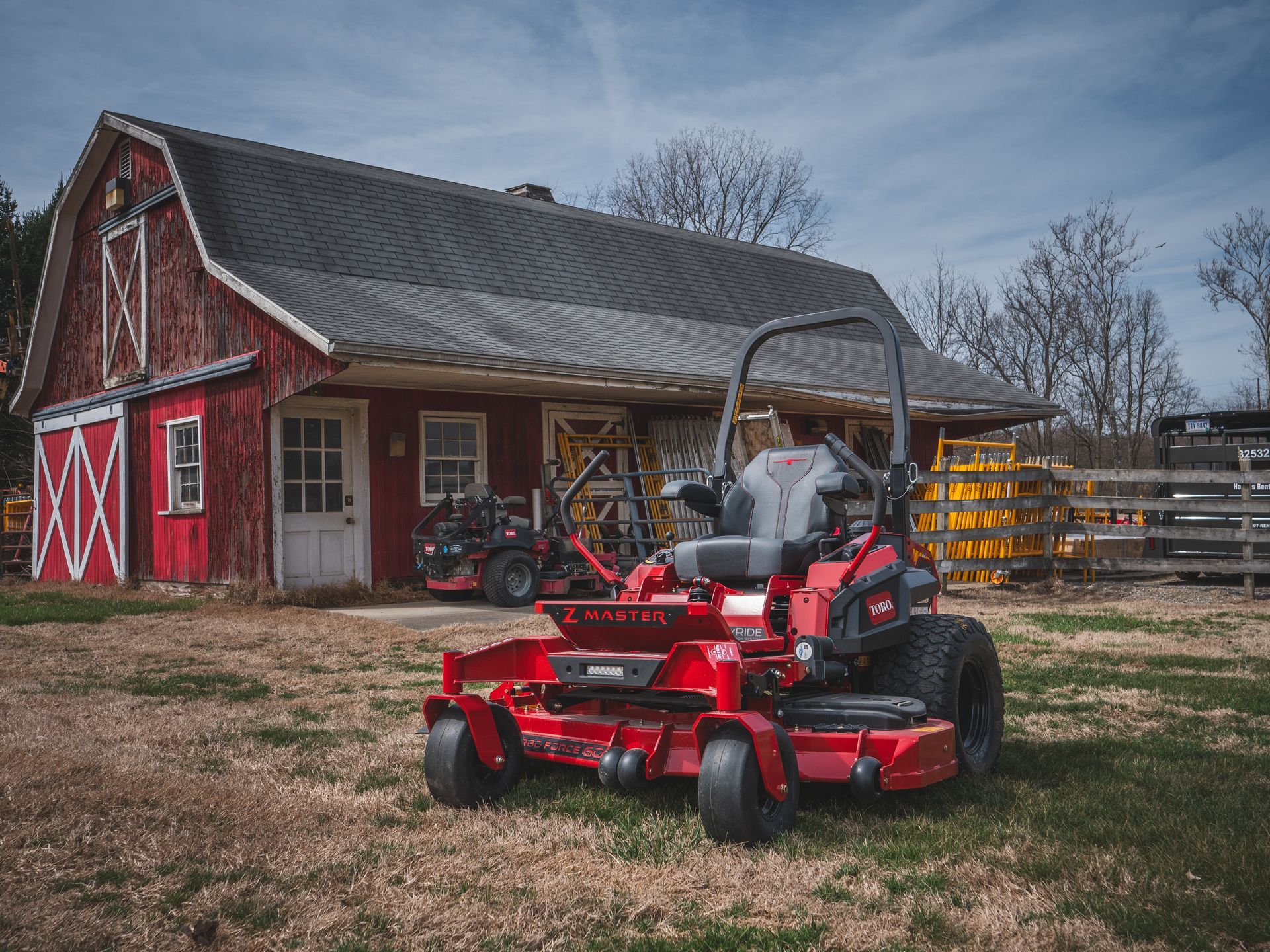 A red lawn mower is parked in front of a red barn.