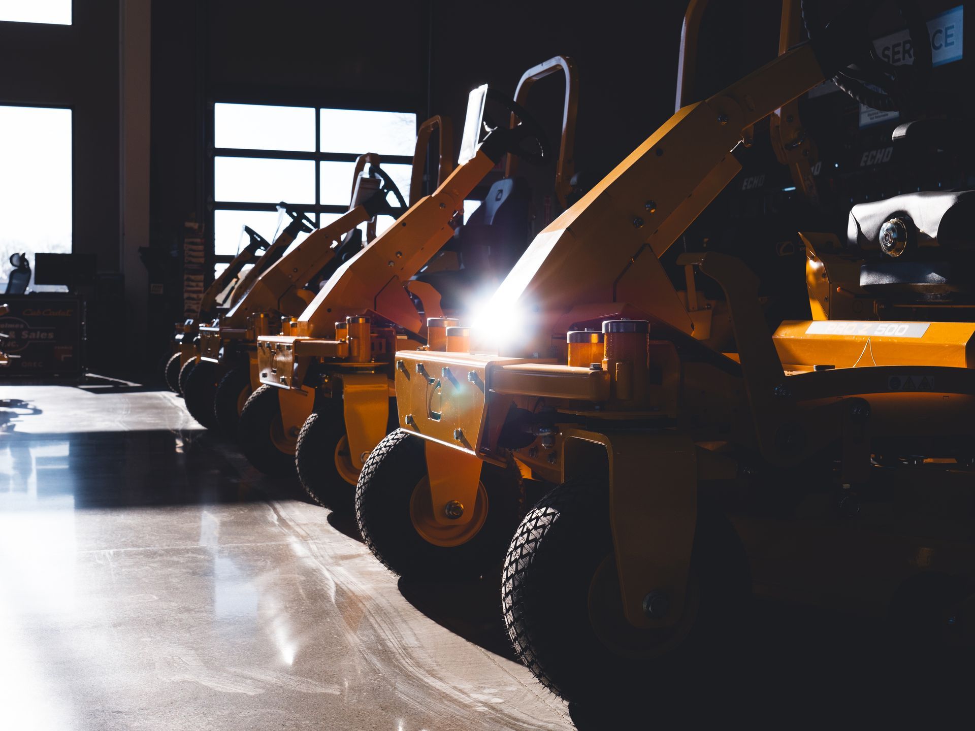 A row of yellow lawn mowers are parked in a garage.