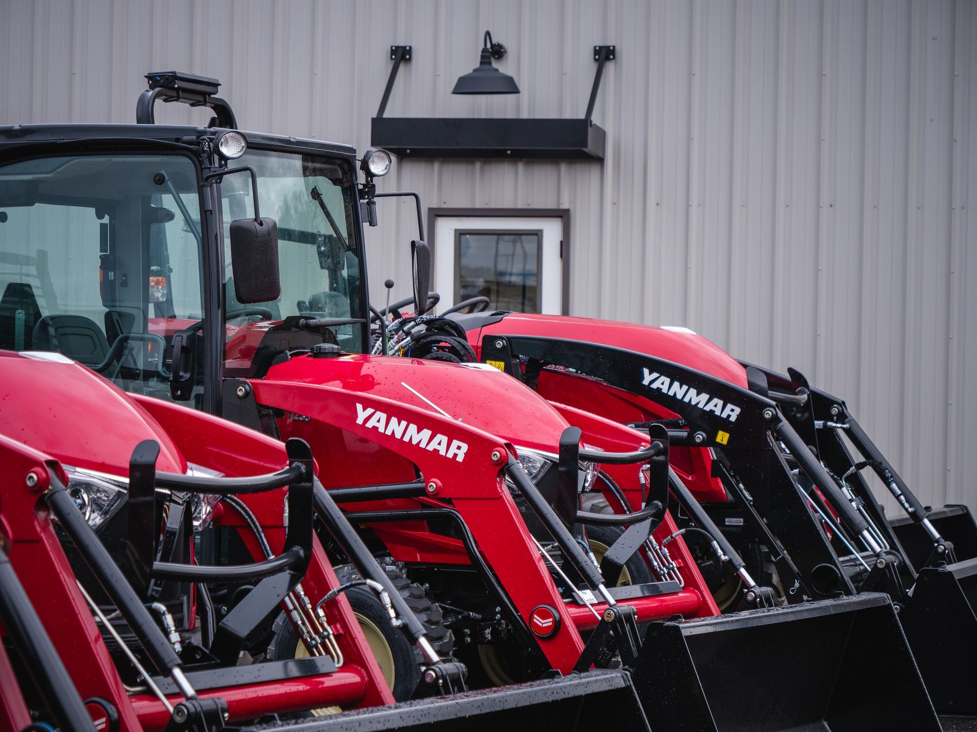 A row of red tractors are parked in front of a building.