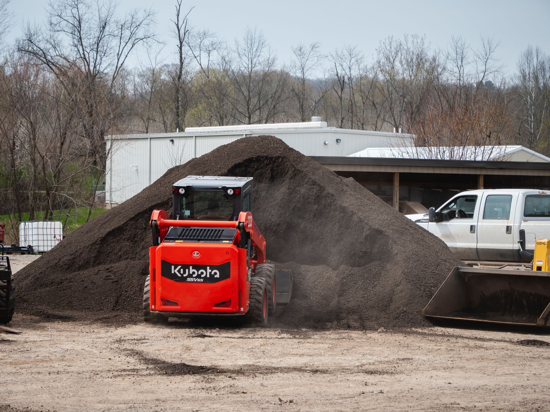 A red kubota skid steer is loading dirt into a pile