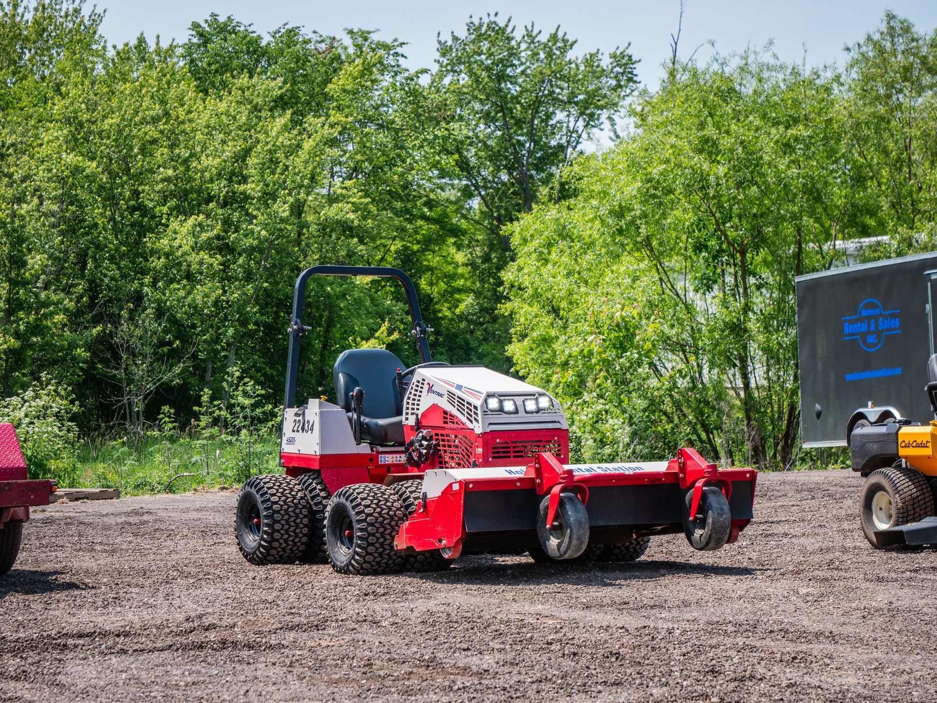 A red and white lawn mower is sitting on top of a dirt field.