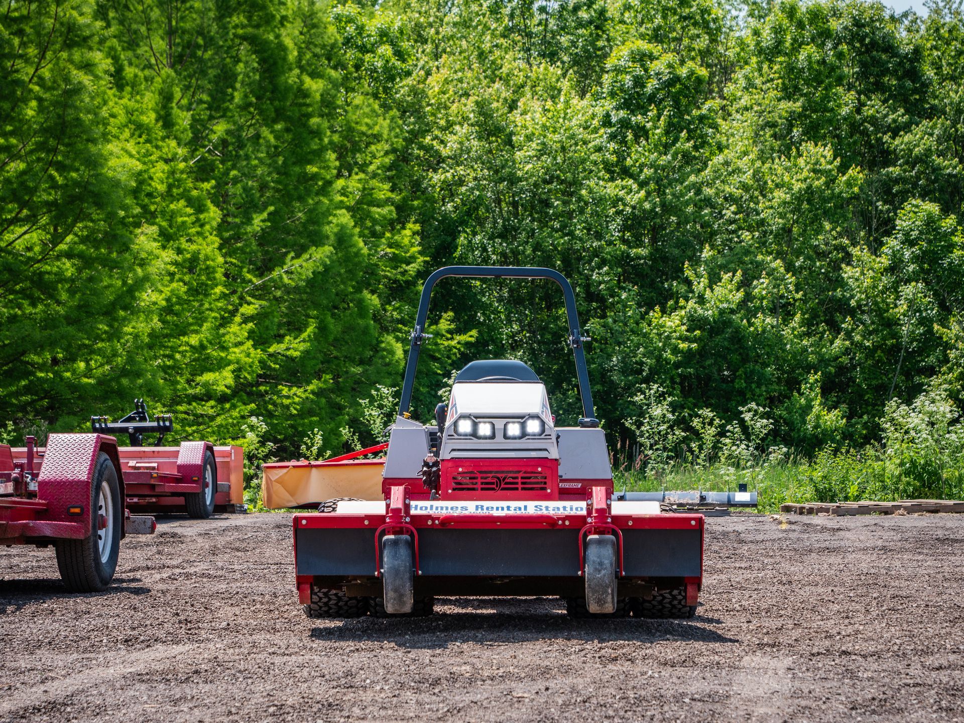 A red and white lawn mower is parked in a dirt field.