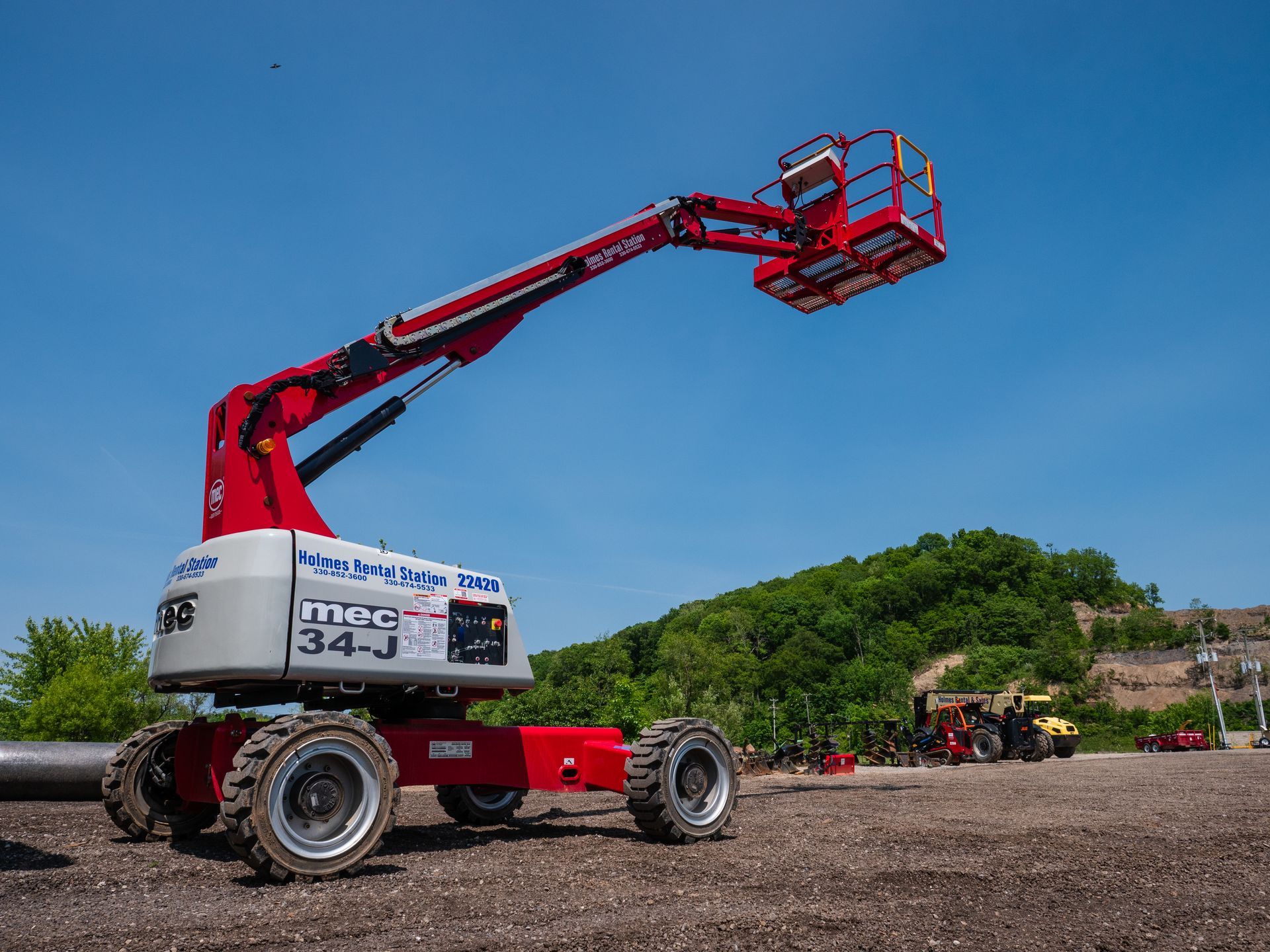A red and white aerial lift is sitting on top of a dirt field.