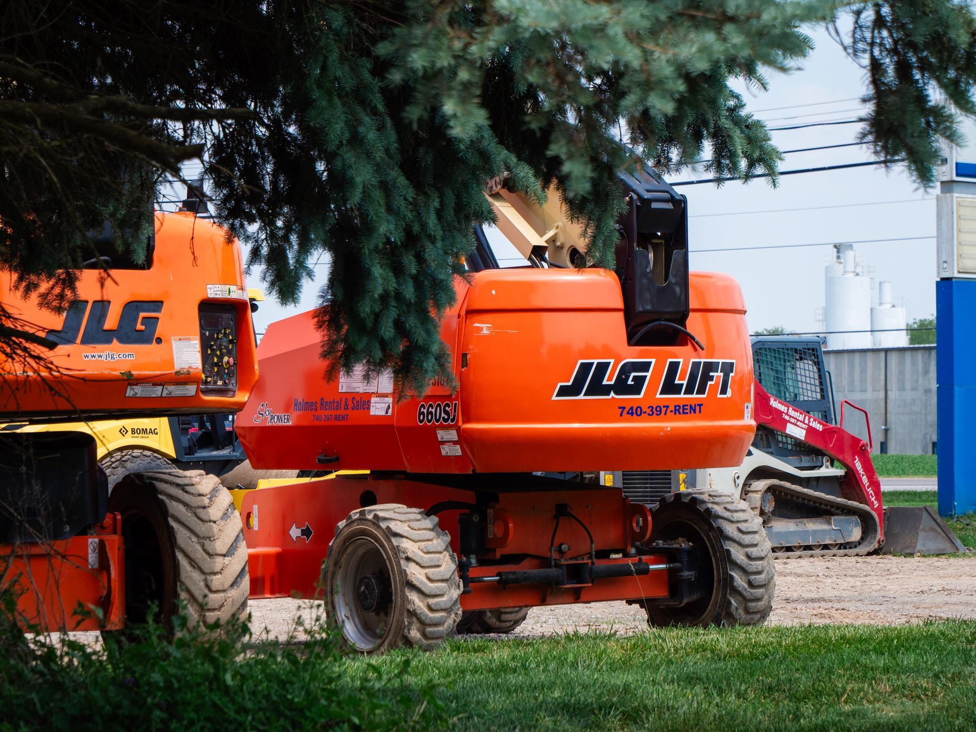 An orange jlg lift is parked under a tree