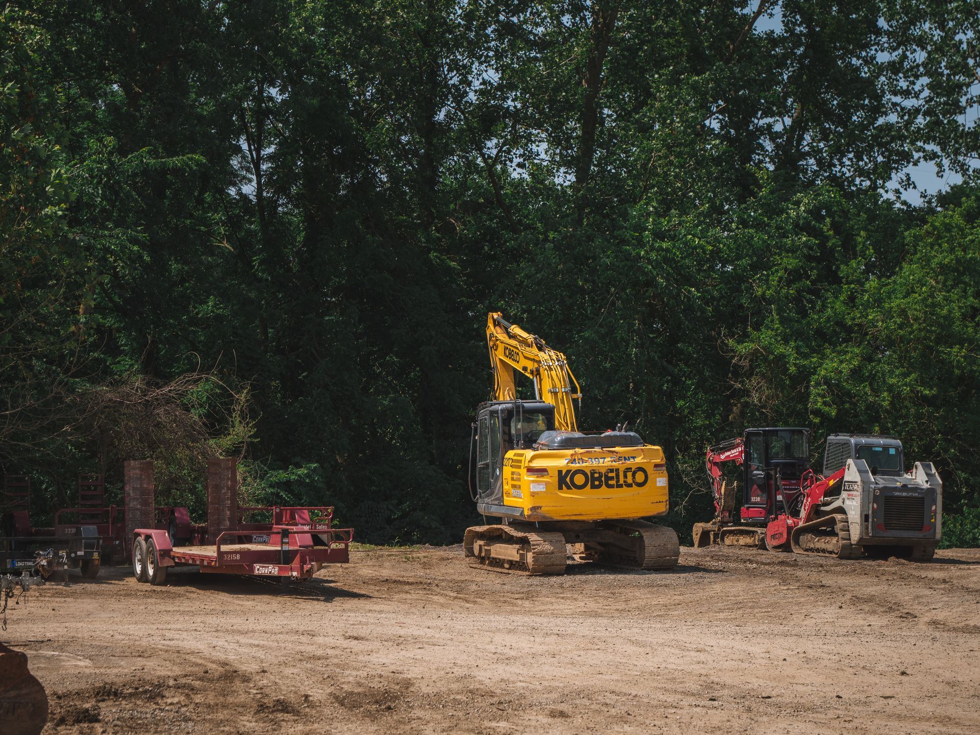 A yellow kobelco excavator is parked in a dirt lot.