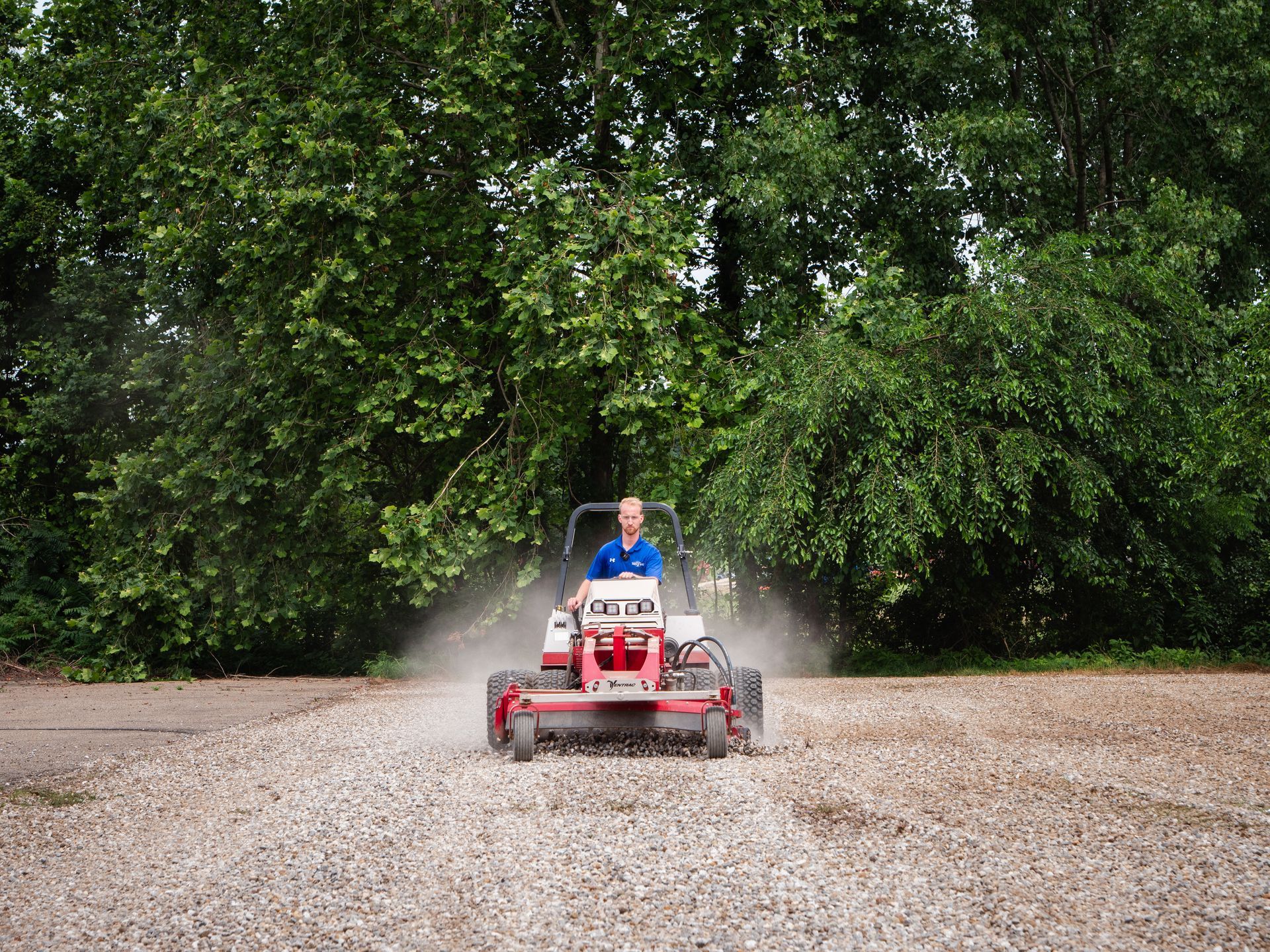 A man is riding a lawn mower on a gravel road.