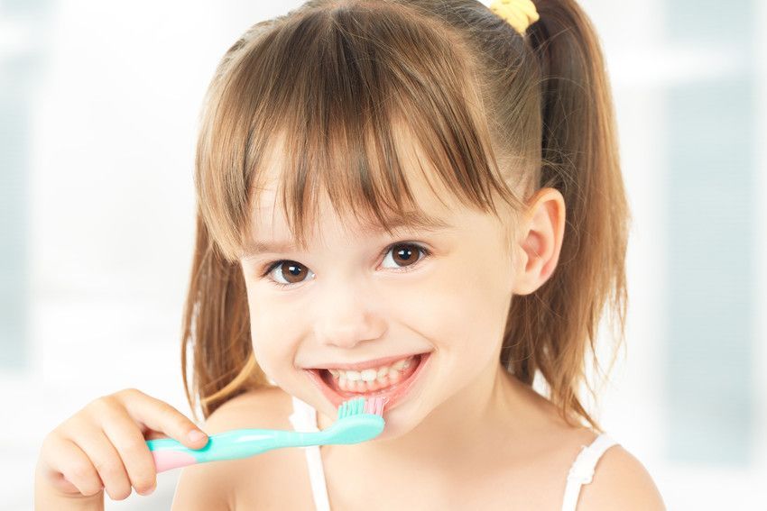 A little girl is brushing her teeth with a toothbrush.