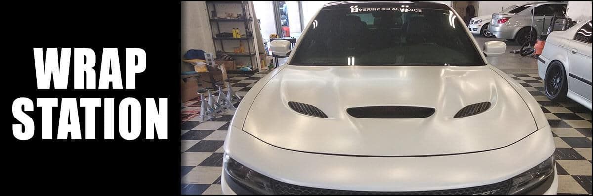 A white car is parked in a garage next to a sign that says wrap station.