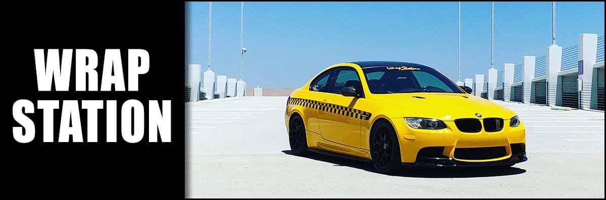 A yellow car is parked in front of a sign that says wrap station