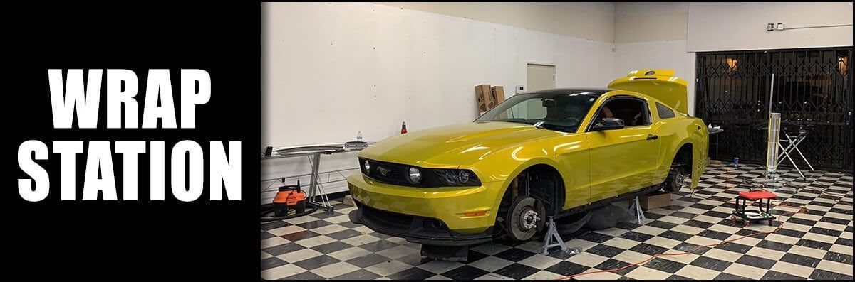 A yellow mustang is sitting in a garage with the hood up.