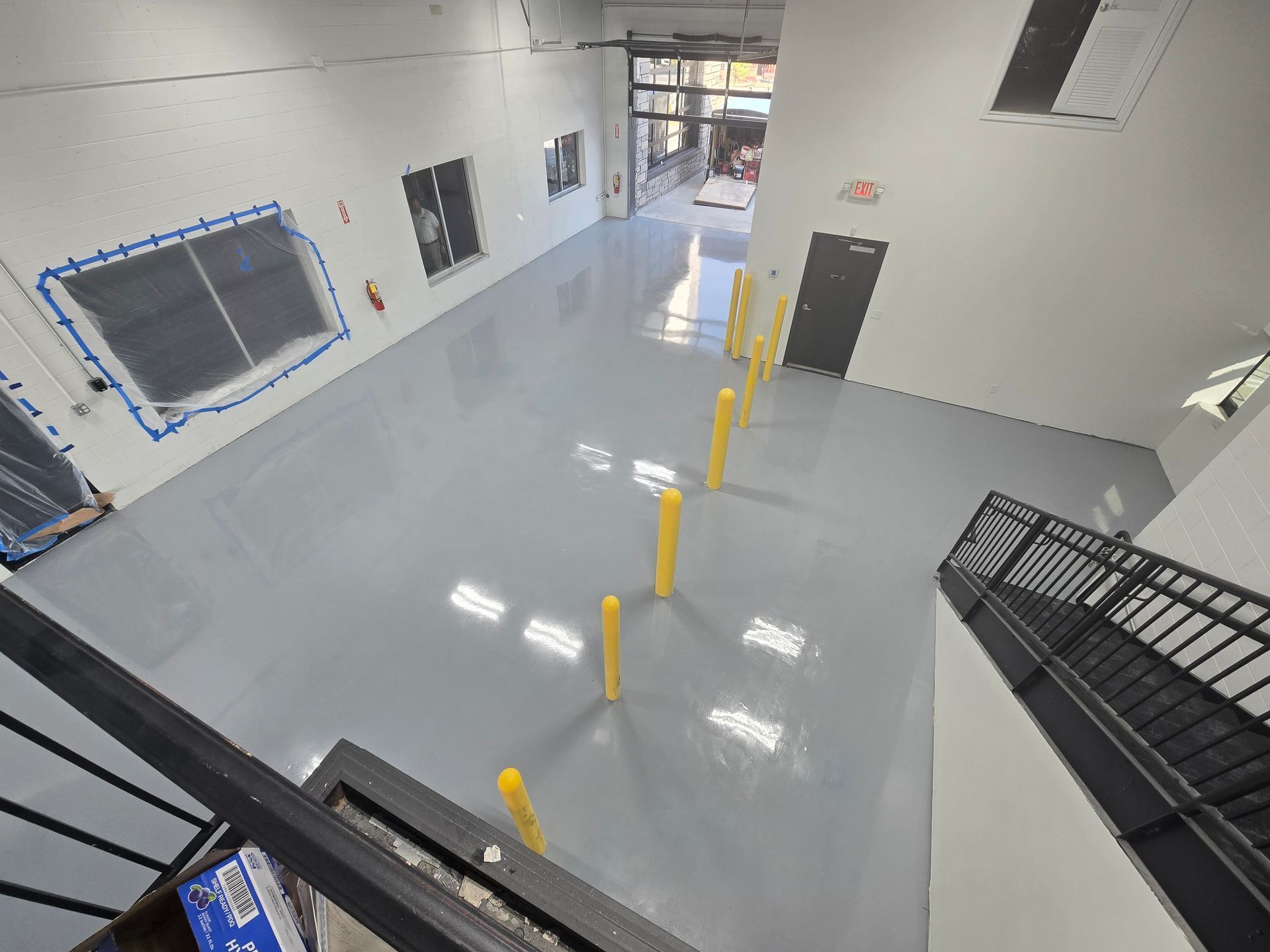 View of an open, gray-floored room with yellow bollards and a staircase.