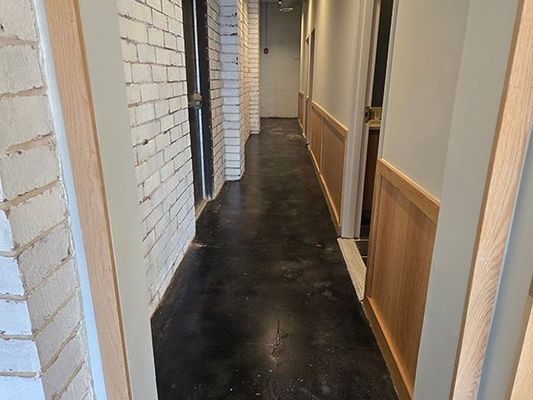 Narrow hallway with brick wall on left, wood paneling on right, dark floor, leading to a door at the end.