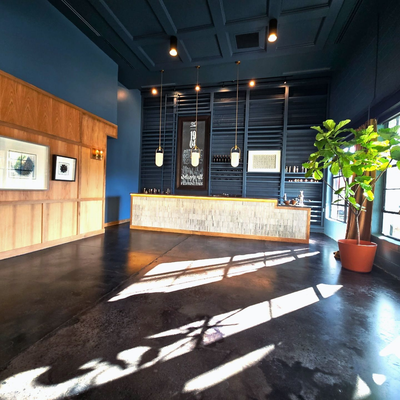 Modern wine bar interior with blue walls, wood accents, and concrete floor; sunlight streams through the window.