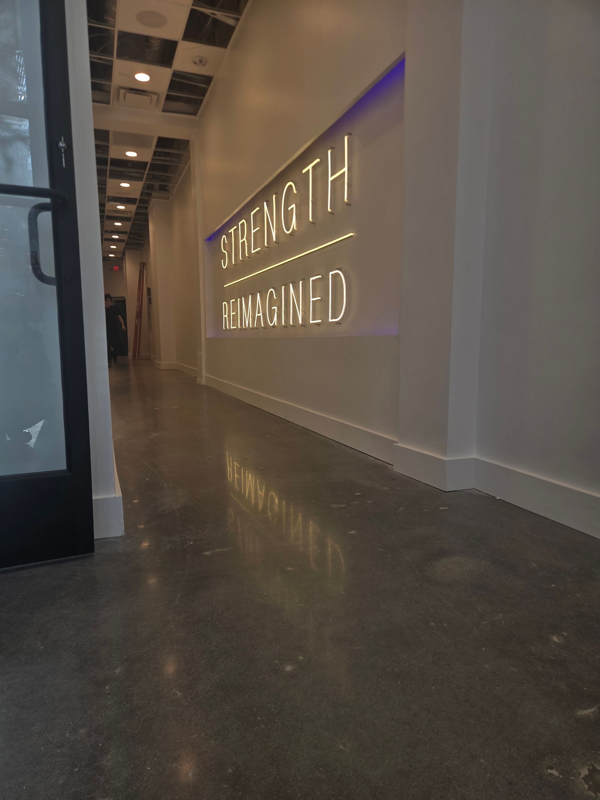 A long hallway with the words STRENGTH REIMAGINED lit up on the wall, polished concrete floor.