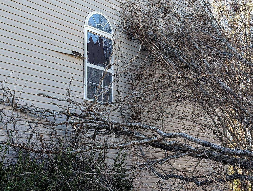 A house with a broken window and a tree in front of it.