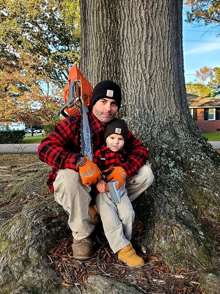 A man and a child are sitting next to a tree holding a chainsaw.