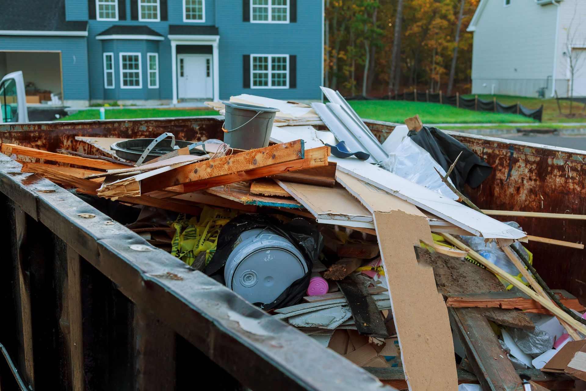 Dumpster overflowing with construction debris in front of a blue house.