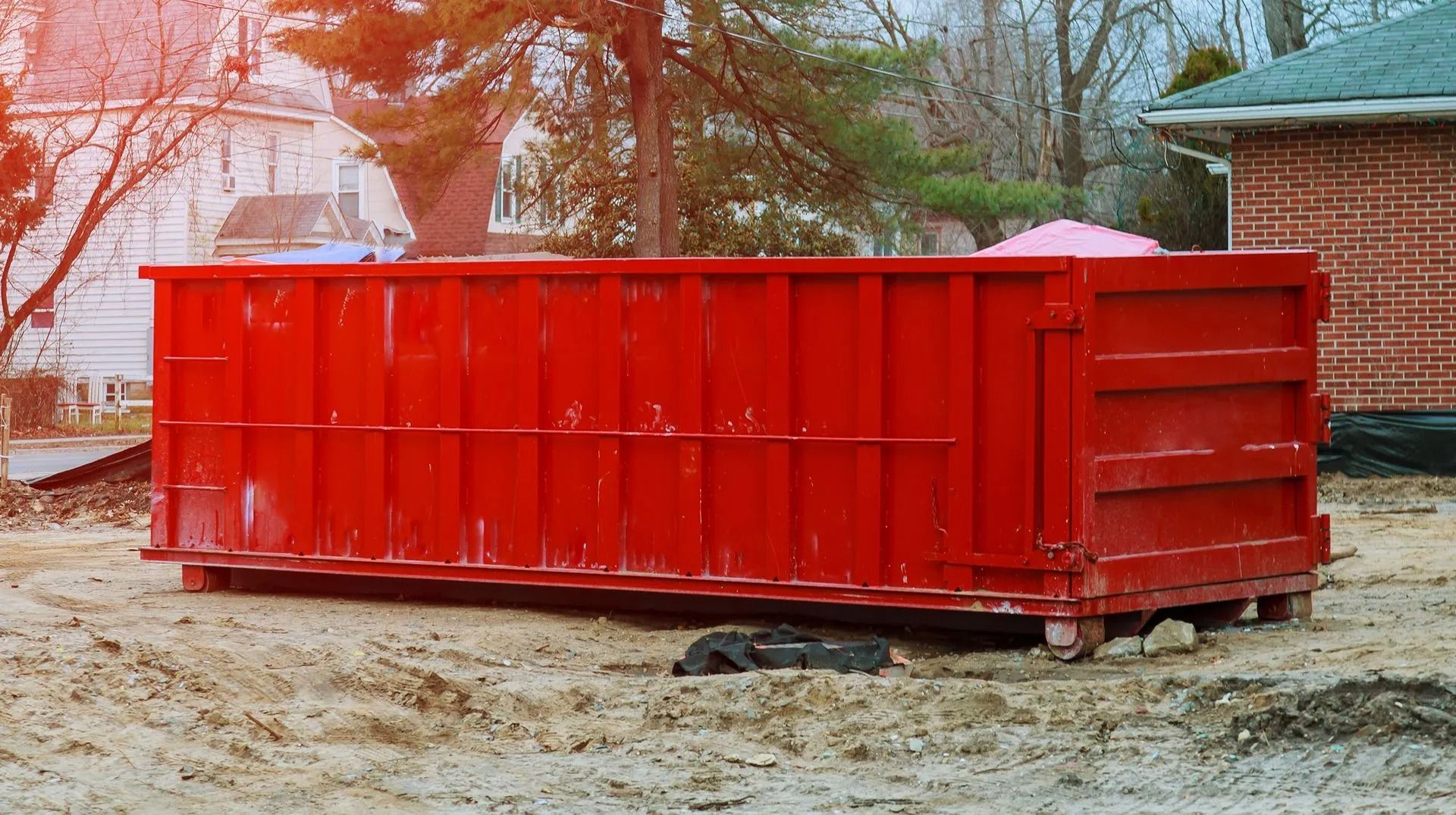 Red dumpster on a construction site; houses and trees in the background.
