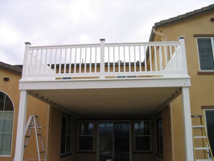 White-railed patio deck under construction on a beige house, with ladders on both sides.