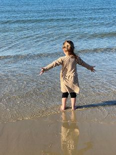 A little girl is standing on the beach with her arms outstretched.