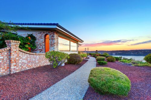 Modern house with stone walls and desert landscaping at sunset, overlooking water and distant hills