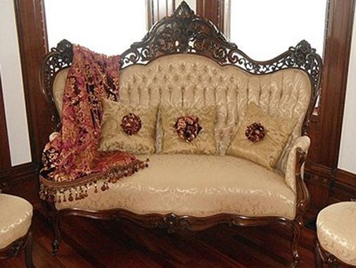 Ornate beige sofa with dark wood frame, decorative pillows, and a patterned throw.